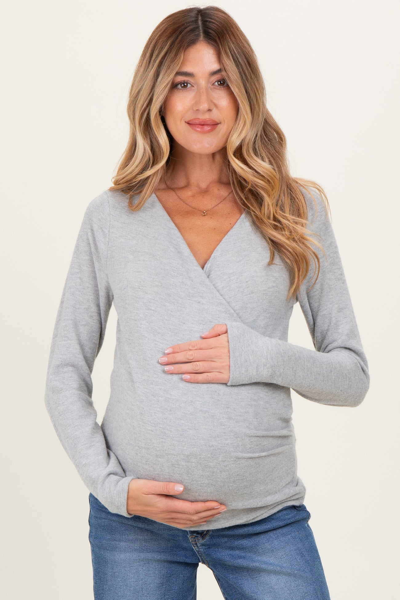 woman wearing a gray long sleeve maternity top and holding her baby bump