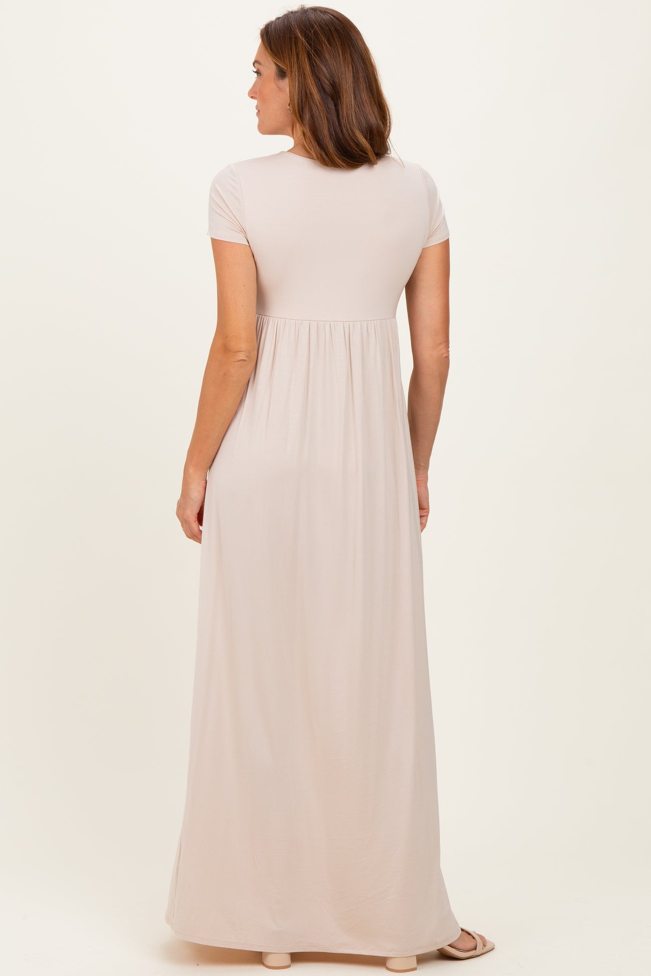 woman wearing a beige short sleeve maxi dress with a flowy skirt seen from the back