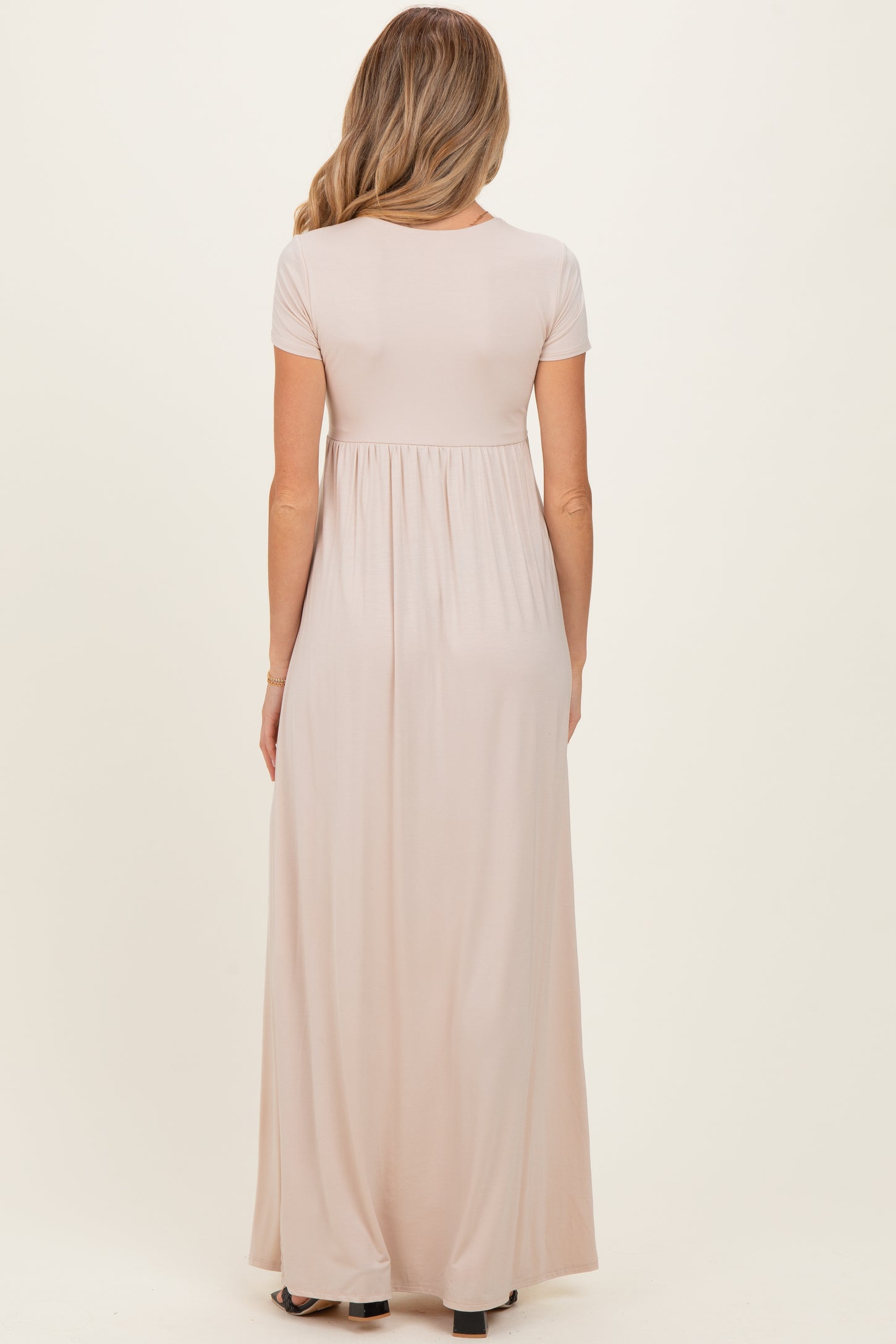 woman wearing a light pink short sleeve maternity maxi dress, showing waistline and flowing skirt from the back
