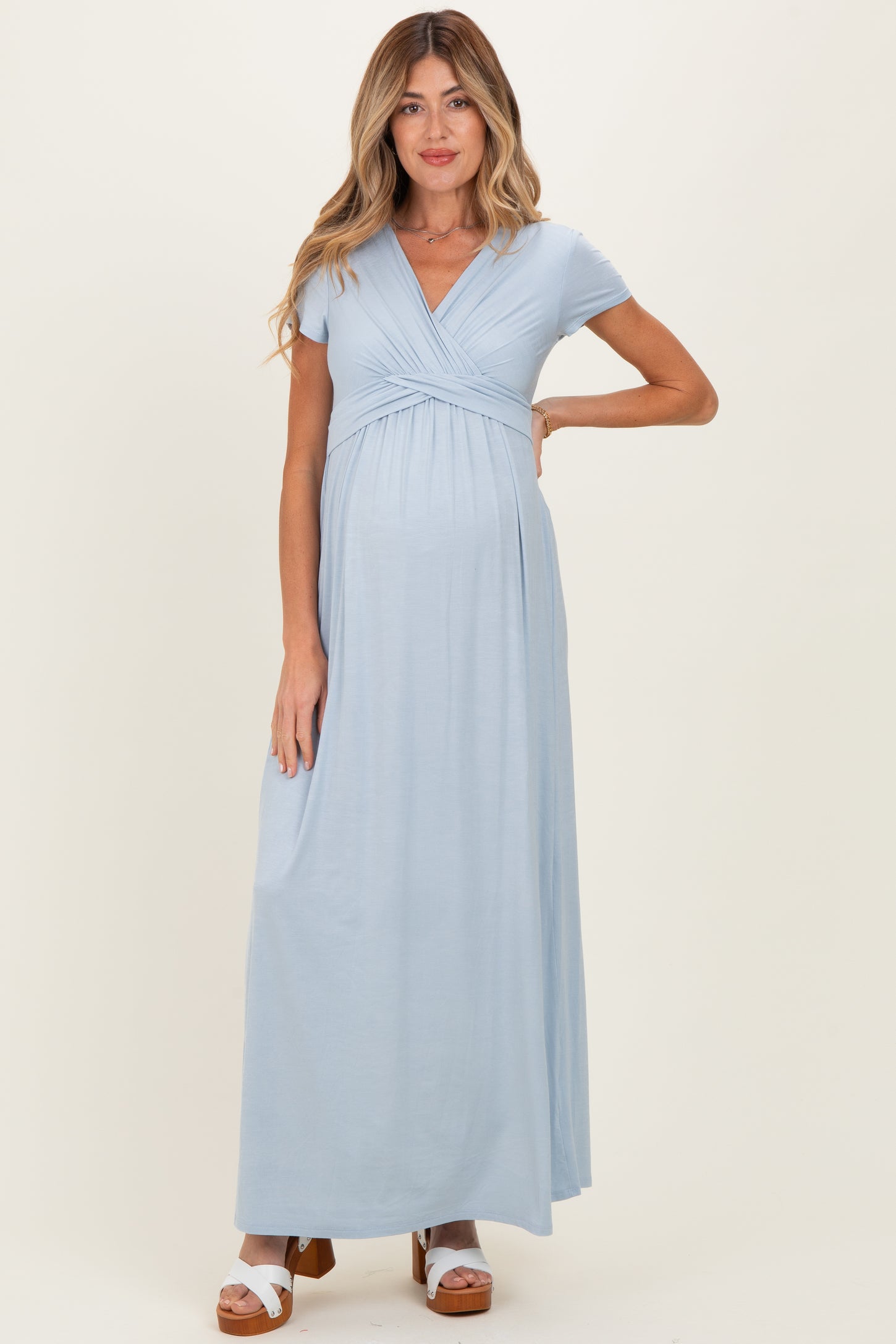 woman wearing a light blue maternity maxi dress with a wrapped bodice and short sleeves, showing her baby bump