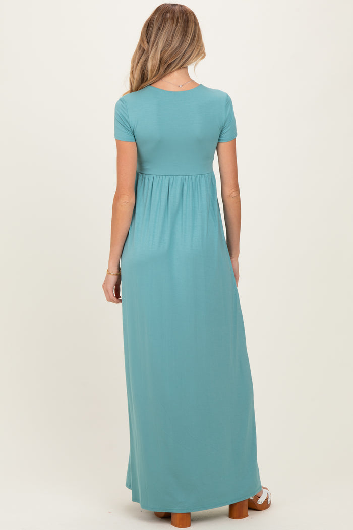 woman wearing a teal short sleeve maxi maternity dress with a fitted bodice and flowing skirt, showing her baby bump
