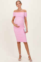 woman wearing a pink off-the-shoulder maternity dress with ruching and holding her baby bump