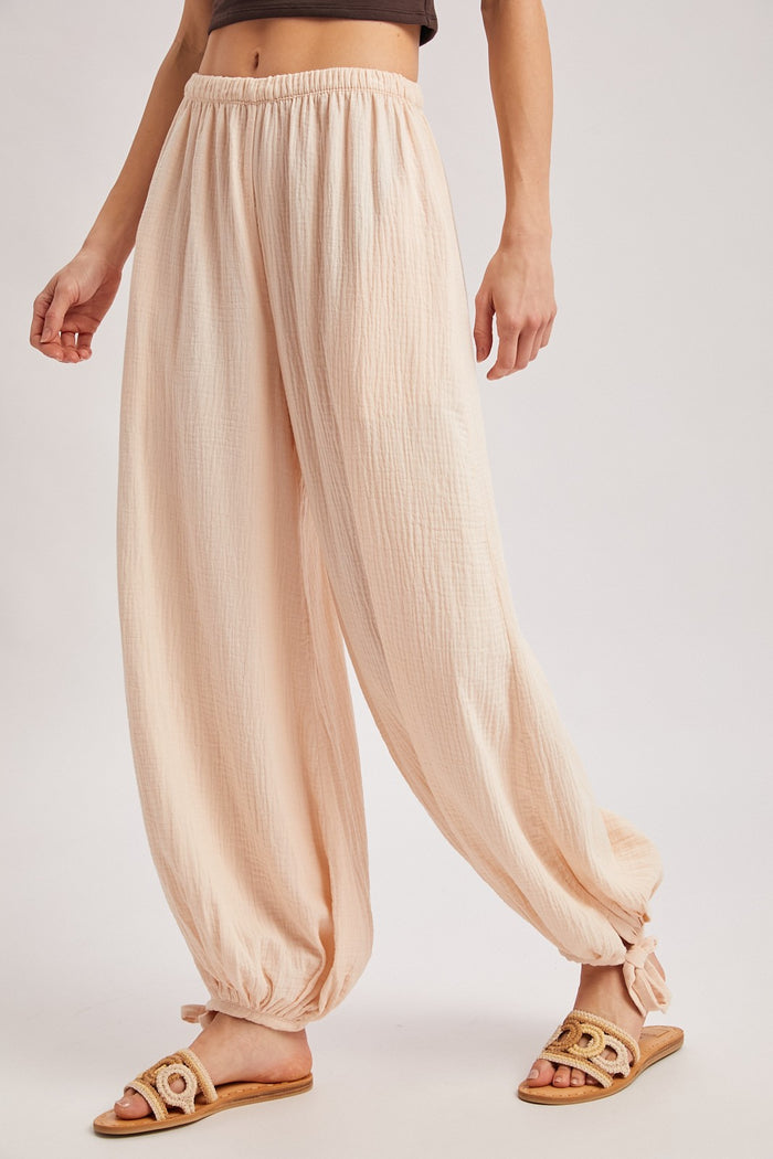 woman wearing light pink loose-fit harem pants with gathered ankle ties and flat sandals