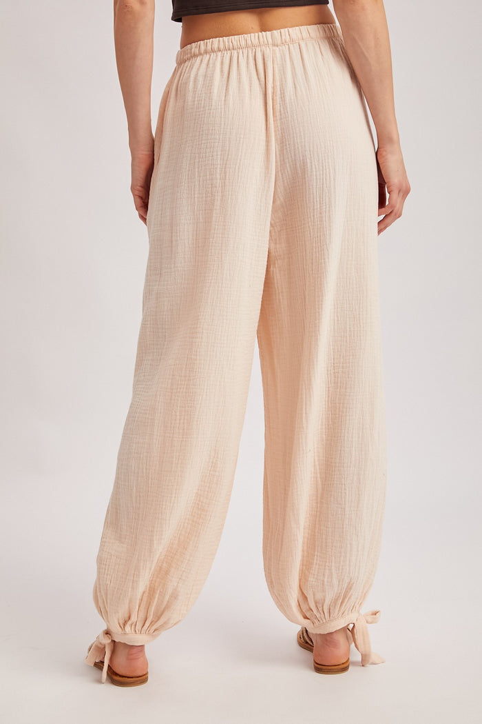 woman wearing light pink loose-fitting pants with elastic waistband and adjustable tie at the ankles, seen from behind