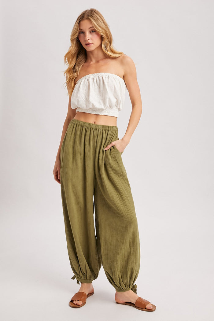 woman wearing a white off-the-shoulder crop top and olive green flowy pants with pockets