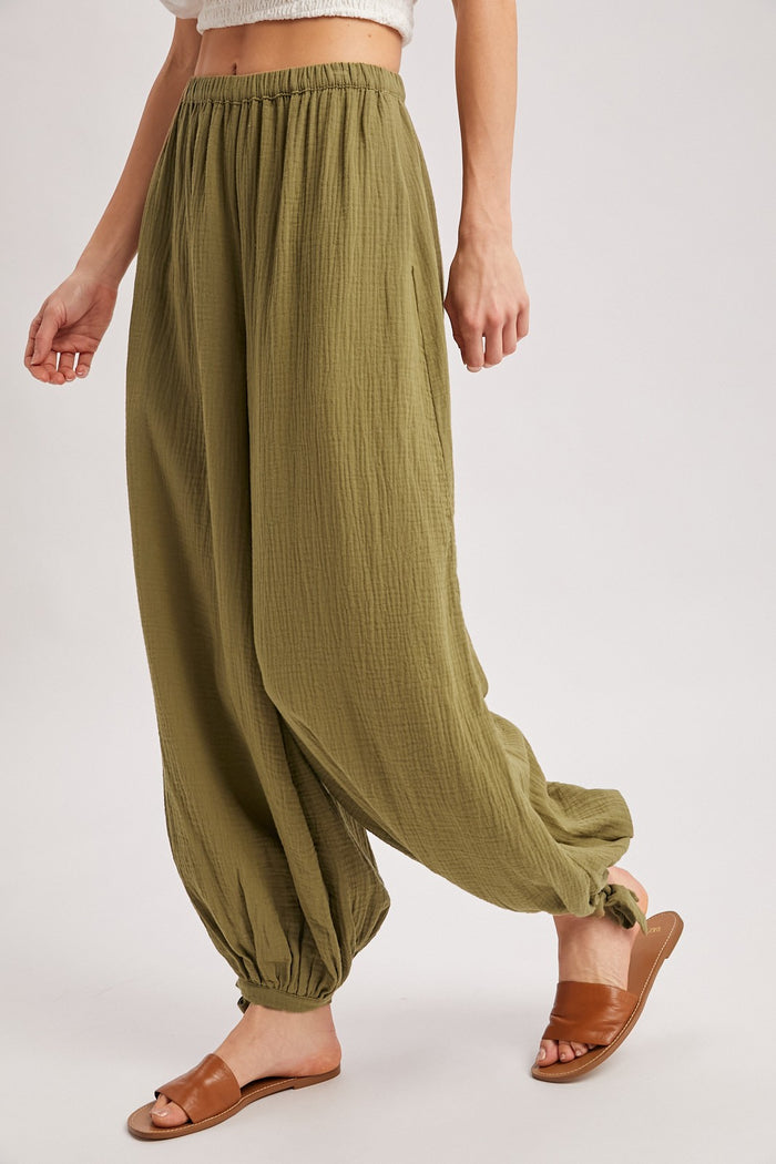woman wearing olive green loose-fitting trousers with elastic cuffs and a high waistband, paired with brown slide sandals