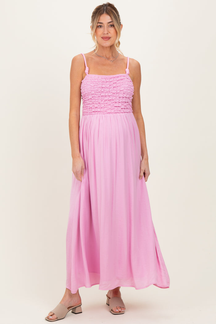 woman wearing a pink maternity maxi dress with smocked bodice and adjustable straps, standing and smiling