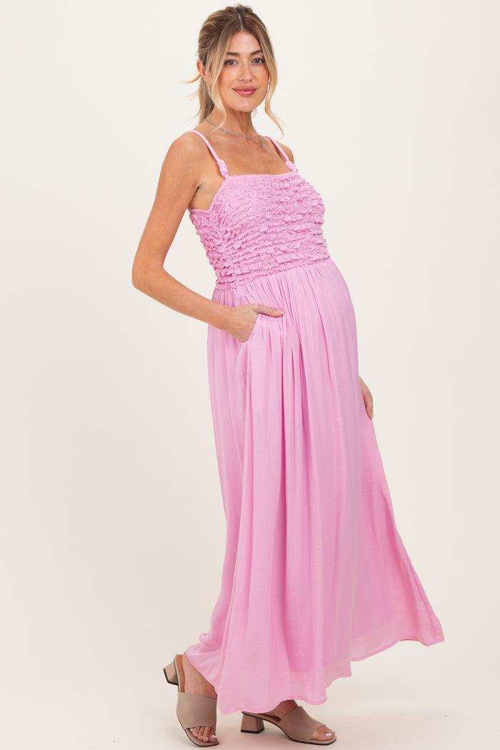 woman wearing a pink maternity maxi dress with ruffled bodice and pockets, showing her baby bump