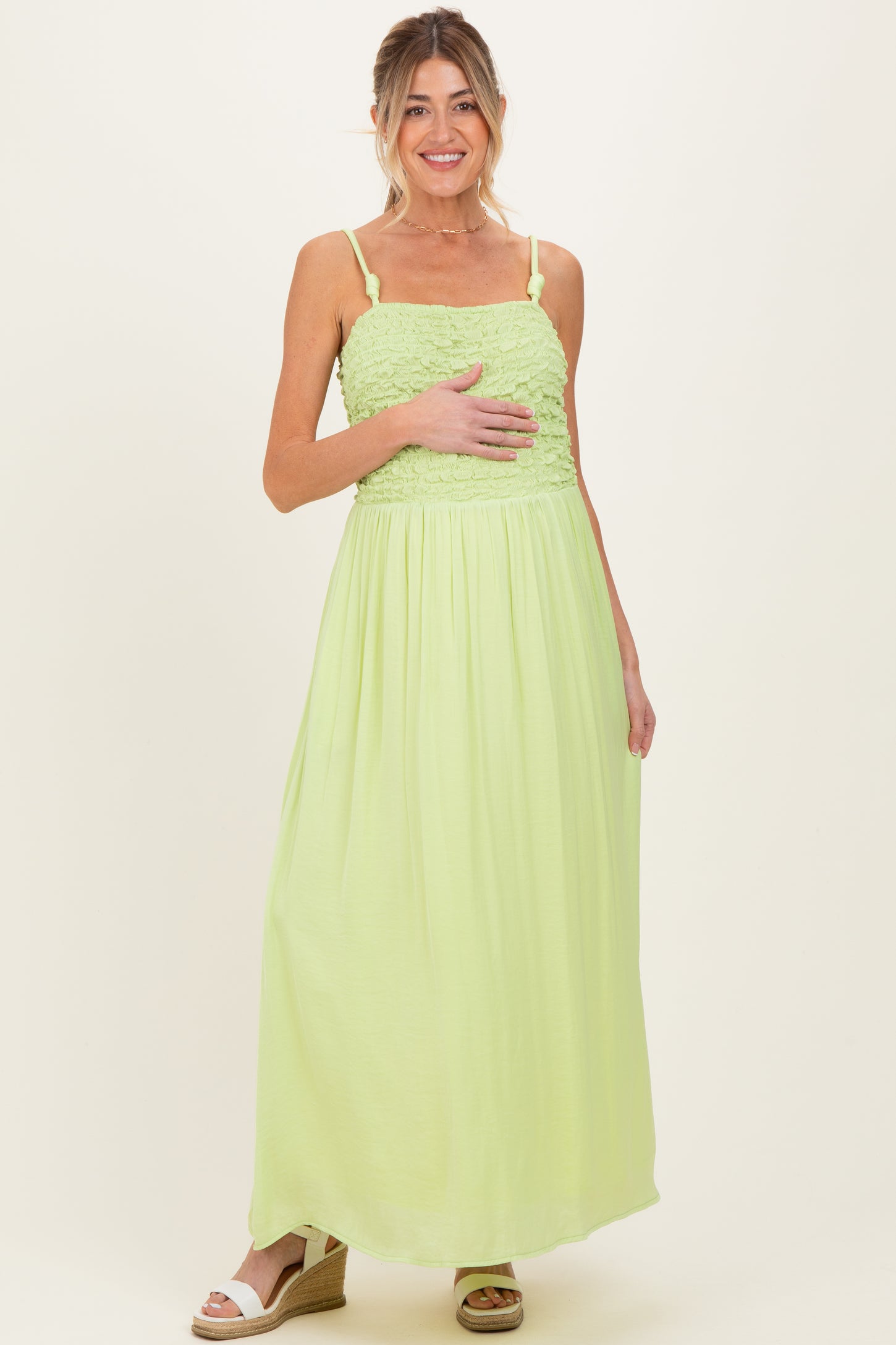 woman wearing a light green maternity maxi dress with smocked bodice and holding her baby bump