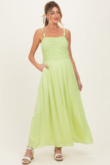 woman wearing a light green maternity maxi dress with smocked bodice and adjustable straps, standing with hands in pockets