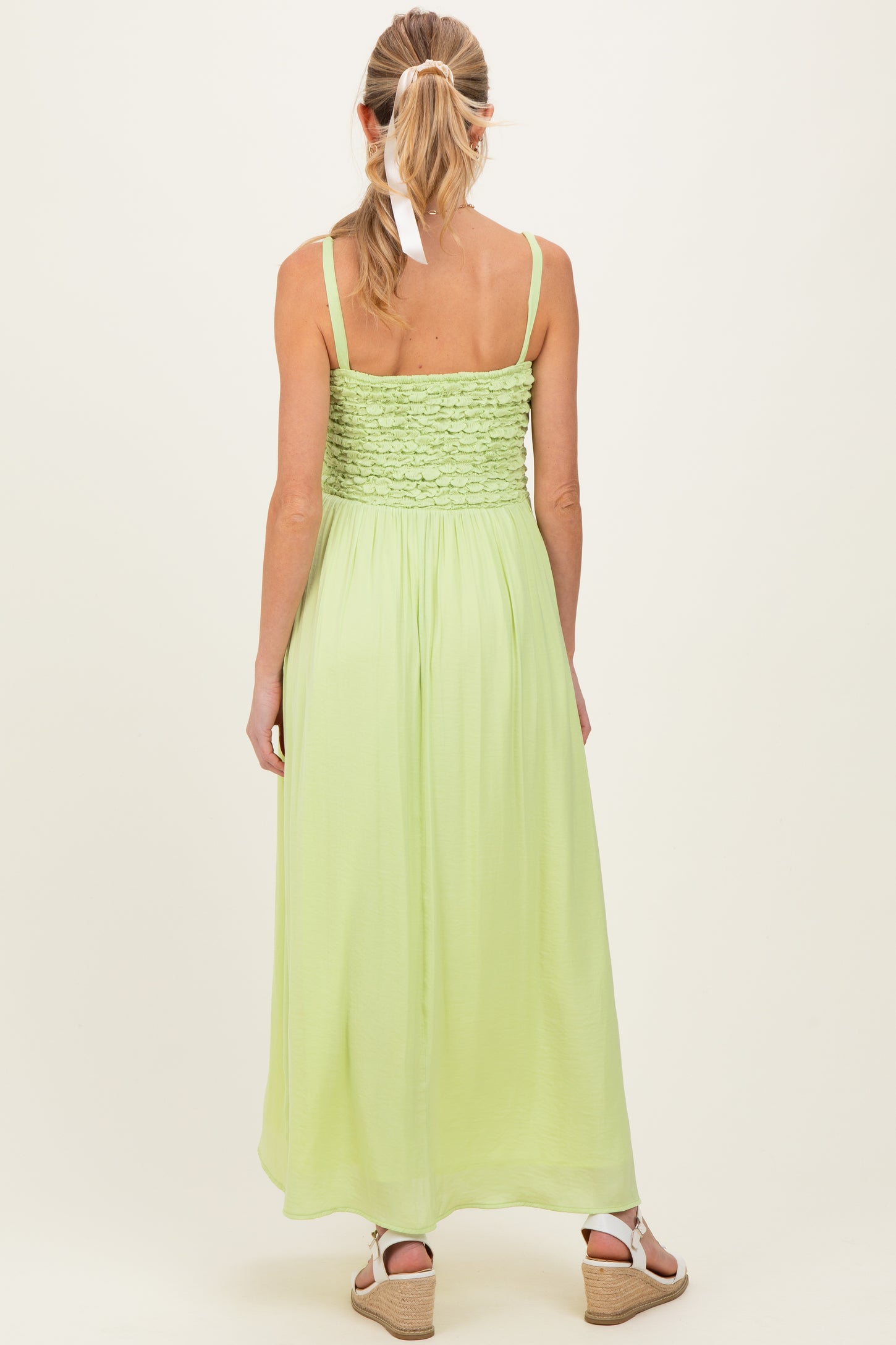 woman wearing a back view of a light green maternity maxi dress with smocked bodice and adjustable straps