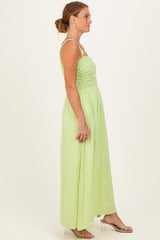 woman wearing a light green maxi dress with a smocked bodice and thin straps, standing in profile