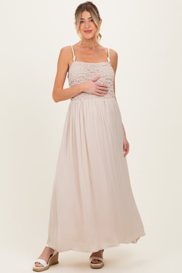 woman wearing a light beige maternity maxi dress with a smocked bodice, holding her baby bump