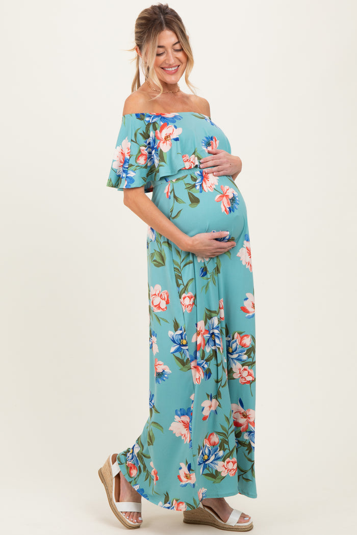 woman wearing a teal off-shoulder floral maternity maxi dress and holding her baby bump