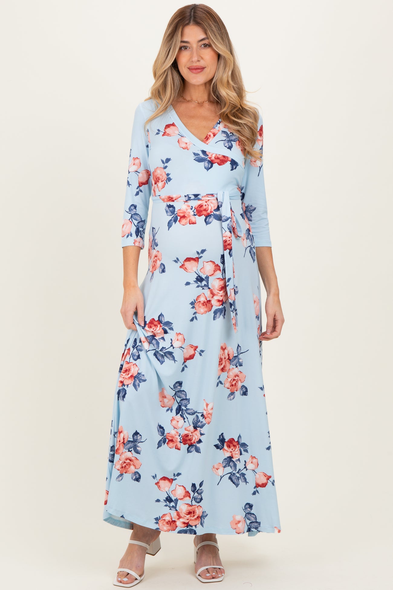 woman wearing a light blue floral maternity maxi dress with three-quarter sleeves and a tie waist, showing her baby bump
