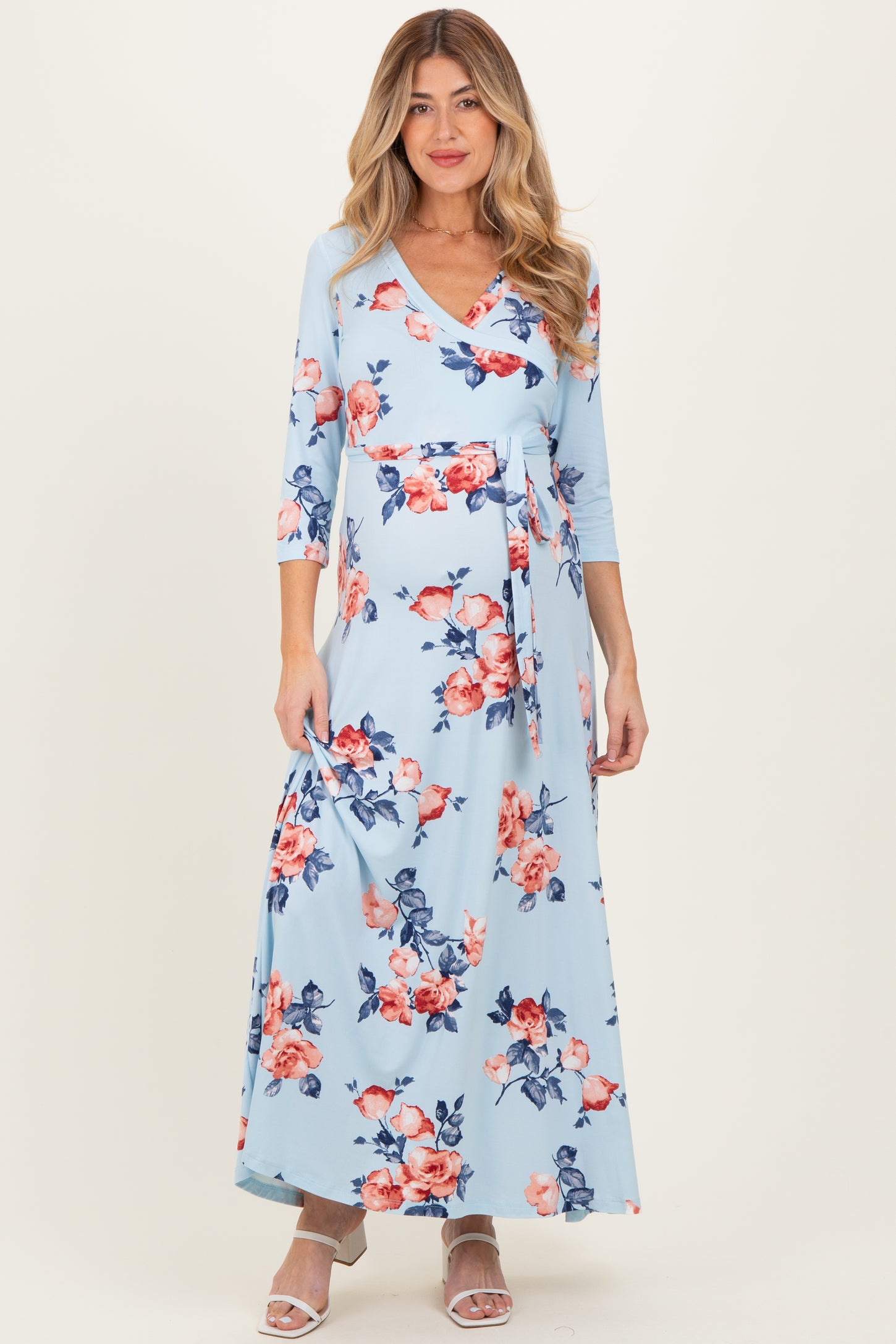 woman wearing a light blue floral maternity maxi dress with three-quarter sleeves and a tie waist, showing her baby bump