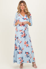 woman wearing a light blue floral maternity maxi dress with three-quarter sleeves and a v-neckline, holding her baby bump