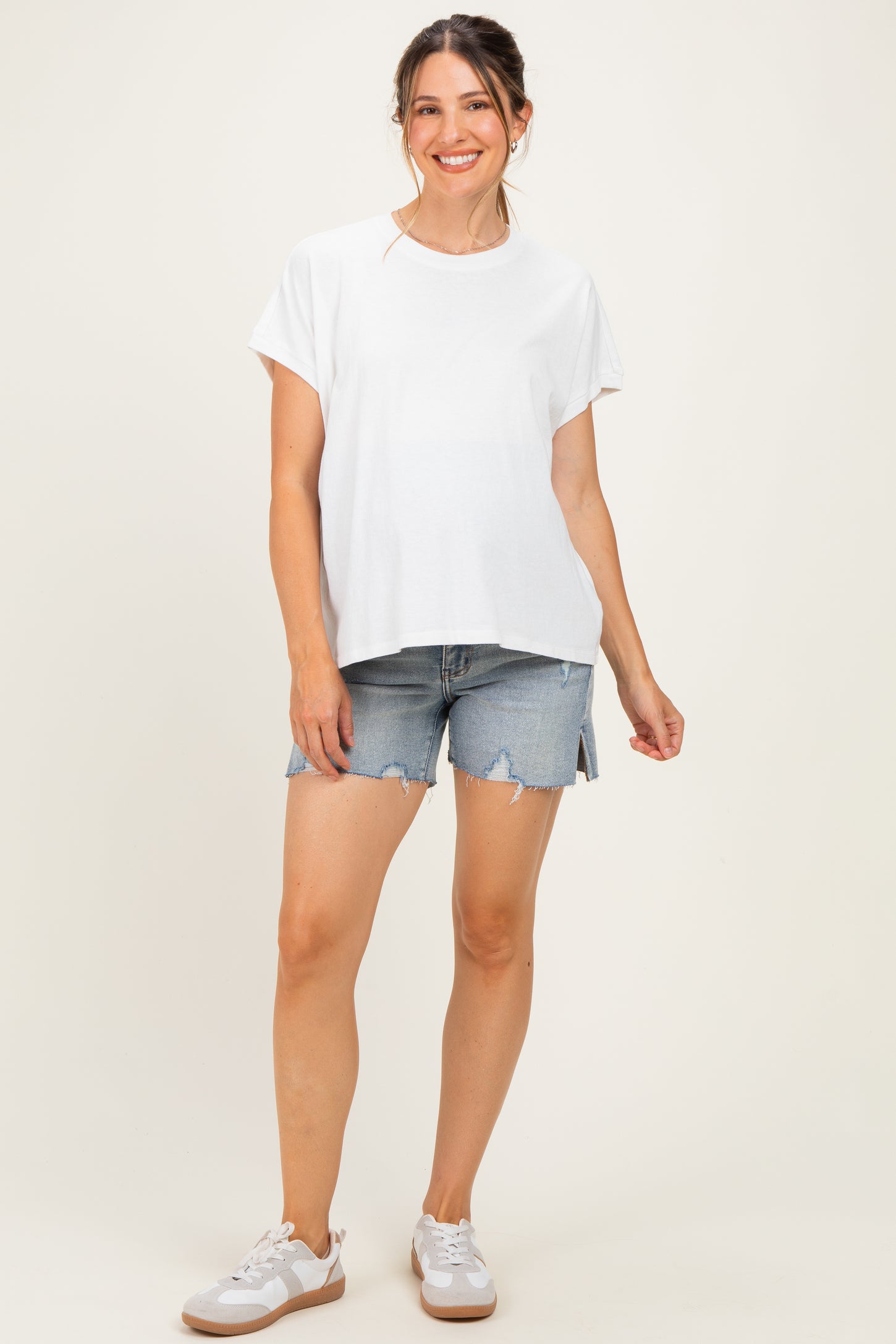 woman wearing a white short sleeve maternity top and denim shorts, showing her baby bump
