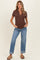 woman wearing a chocolate brown short sleeve maternity top with buttons and blue rolled cuff jeans, standing with hands in pockets