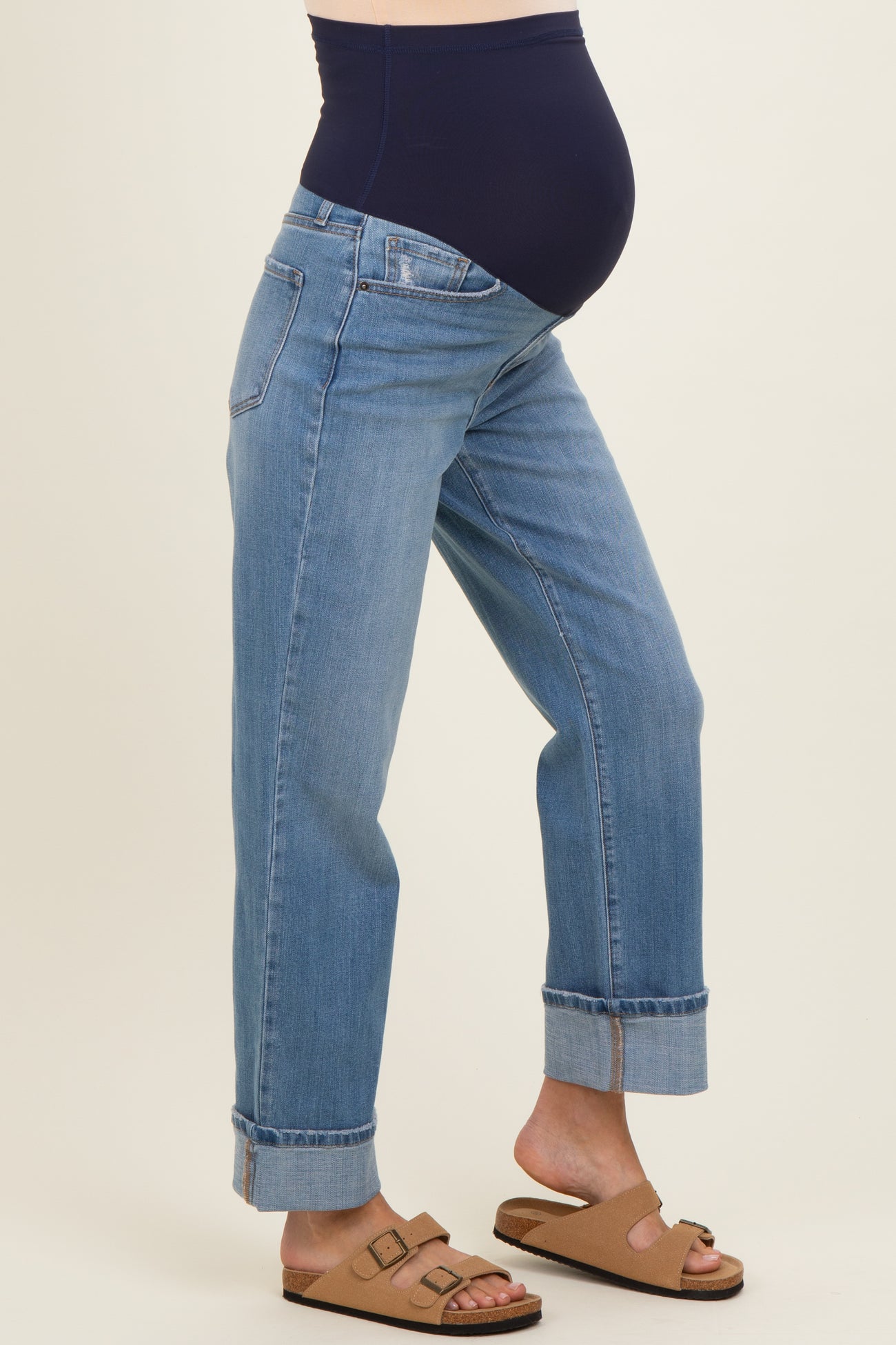 woman wearing a pair of light blue maternity jeans with a navy over-the-bump waistband and rolled cuffs, showing a baby bump