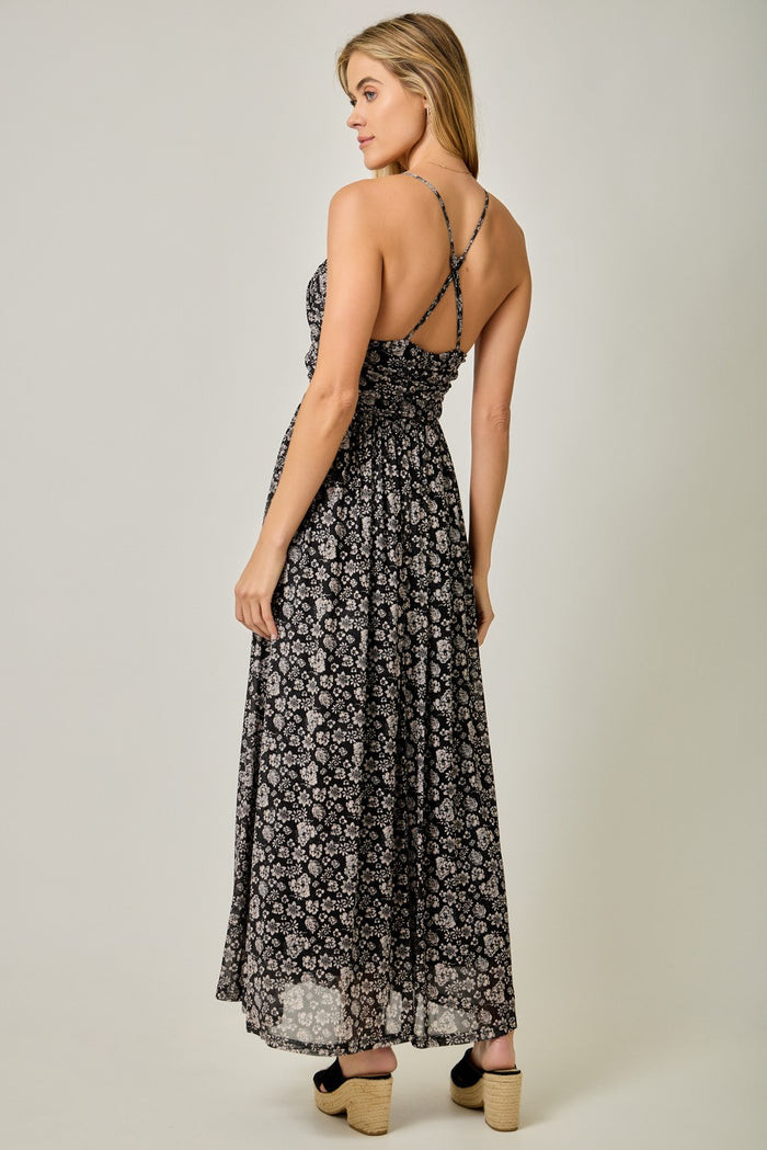 woman wearing a black floral maxi dress with thin straps and a flowy skirt, standing with her back to the camera