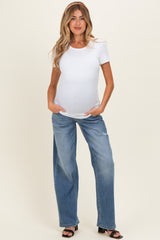woman wearing a white short sleeve maternity top and loose blue maternity jeans, showing her baby bump