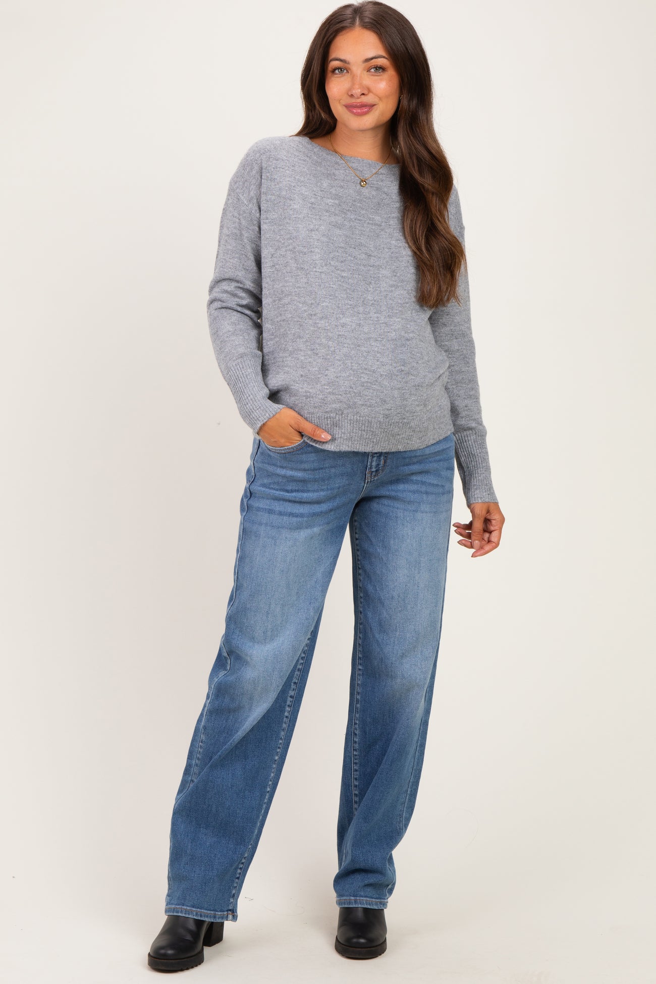 woman wearing a grey maternity sweater with a relaxed fit and blue wide-leg jeans, holding one hand in her pocket