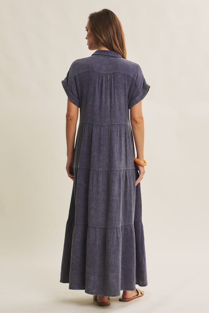 woman wearing a navy blue tiered maxi dress with short sleeves and a collared neckline, shown from the back