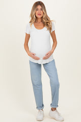 woman wearing a white short sleeve maternity top and holding her baby bump with light blue jeans and white sneakers