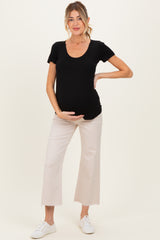 woman wearing a black scoop neck maternity top and holding her baby bump, paired with light beige cropped pants and white sneakers