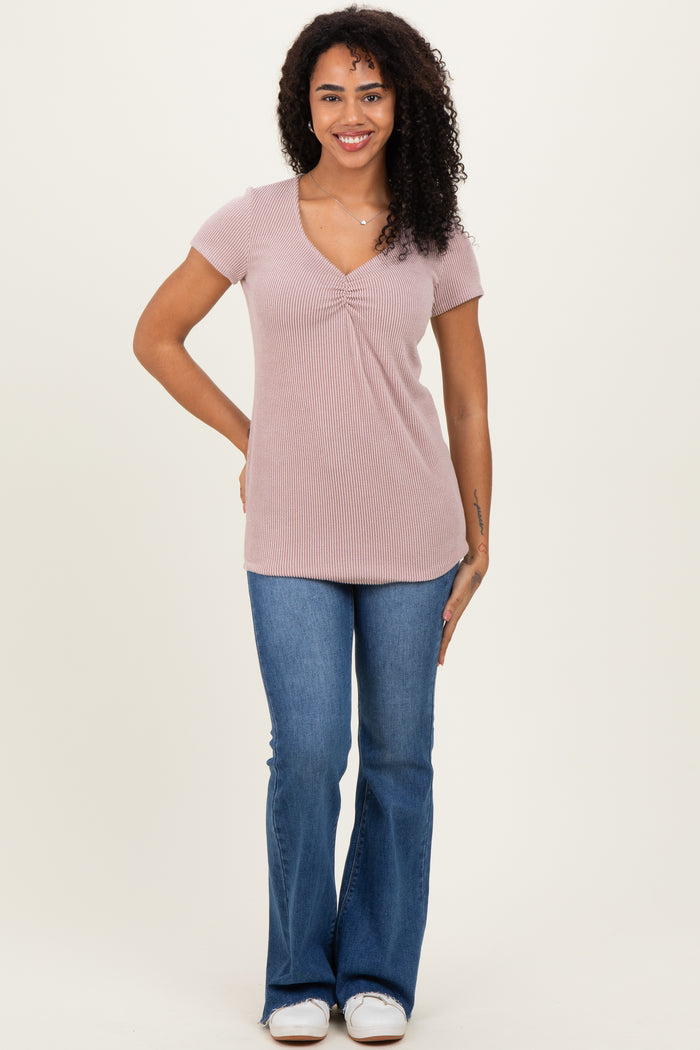 woman wearing a light pink ribbed short sleeve top and blue flared jeans, standing and smiling