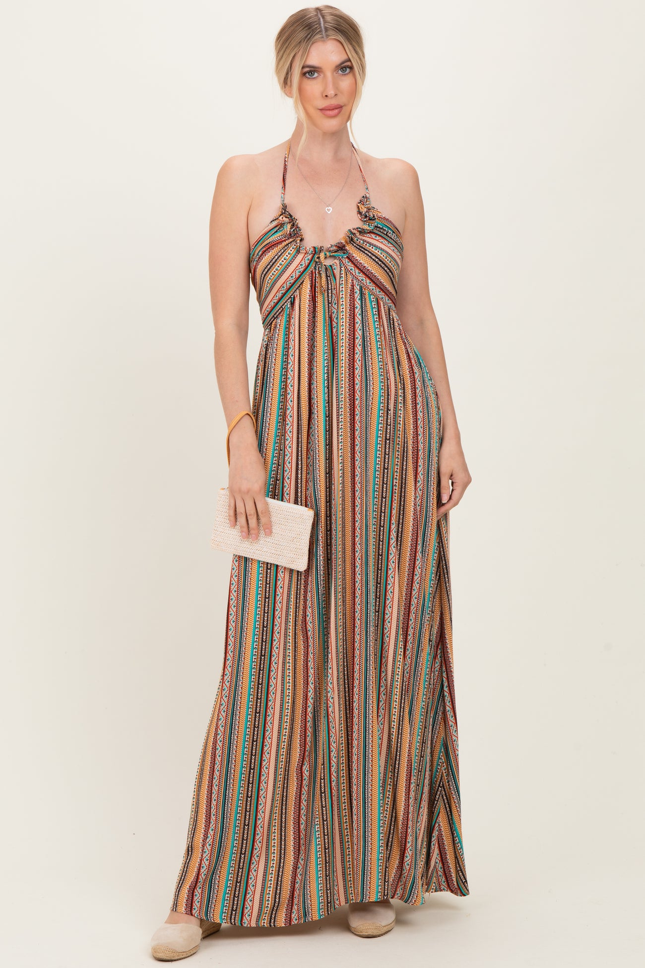 woman wearing a multi-colored striped maxi dress with a halter neckline and holding a small clutch purse