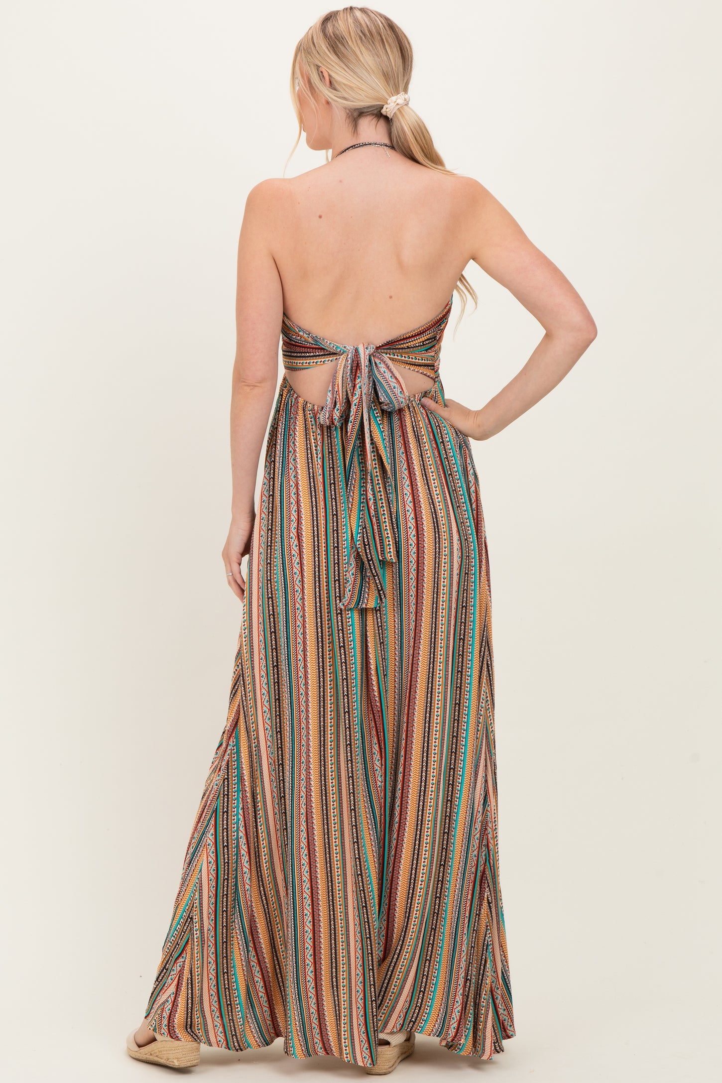 woman wearing a multi-colored striped backless maxi dress with a tie closure at the back