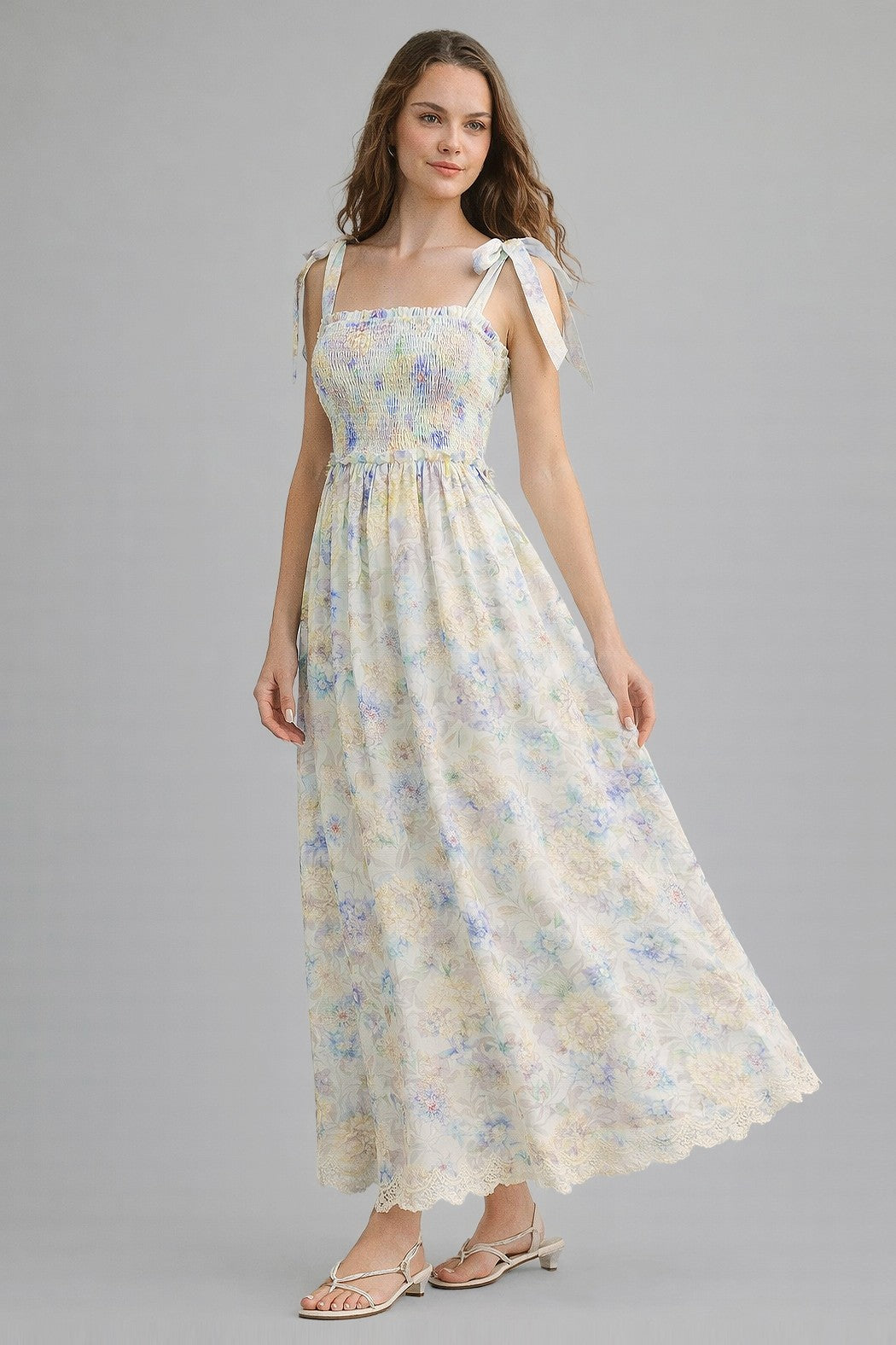 woman wearing a floral maxi dress with smocked bodice and tie straps, standing against a gray background