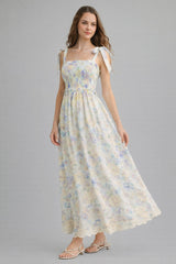 woman wearing a floral maxi dress with smocked bodice and tie straps, standing against a gray background