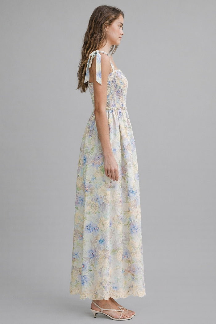 woman wearing a floral maxi dress with adjustable tie straps and a smocked bodice in pastel colors