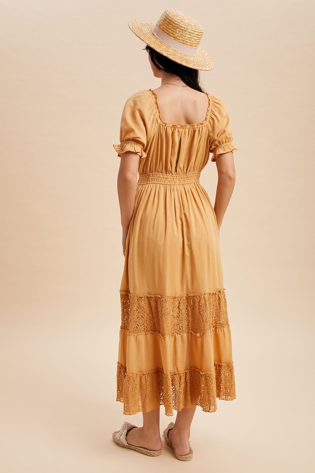 woman wearing a mustard yellow maxi dress with lace detailing and puff sleeves, styled with a straw hat