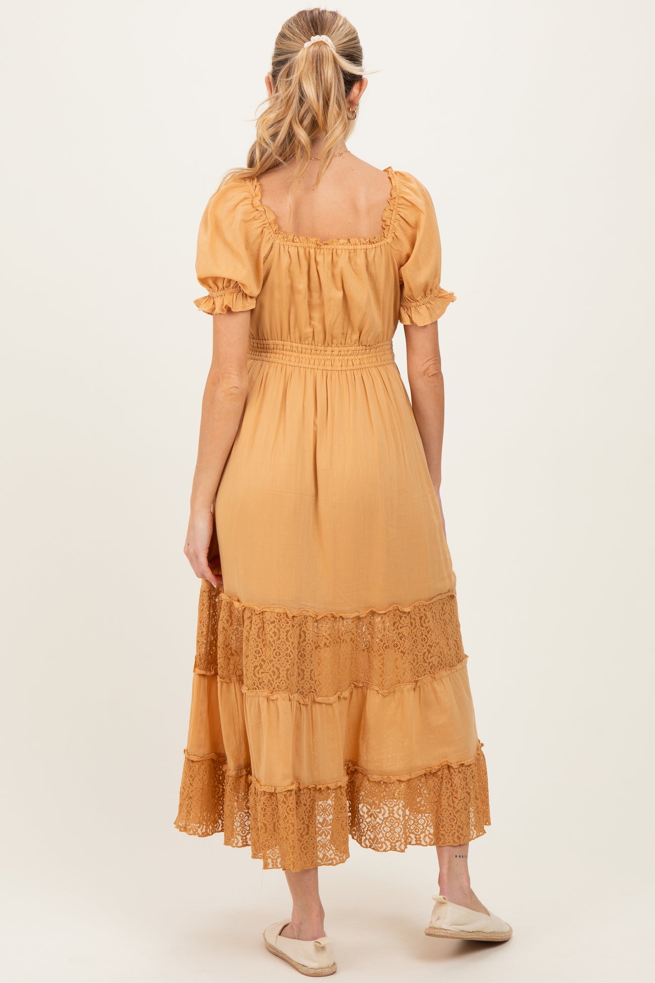 woman wearing a mustard yellow maternity dress with short sleeves and lace detailing on the hem