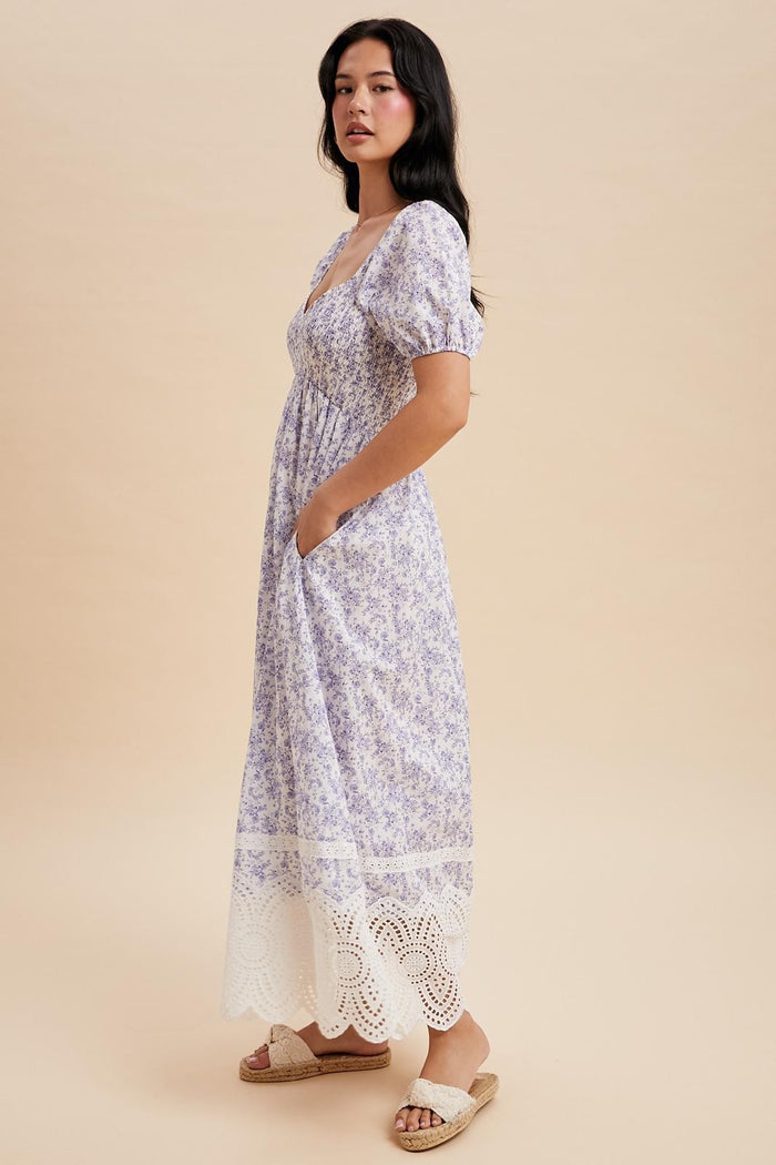 woman wearing a lavender floral maxi dress with puff sleeves and lace trim, standing with hands in pockets