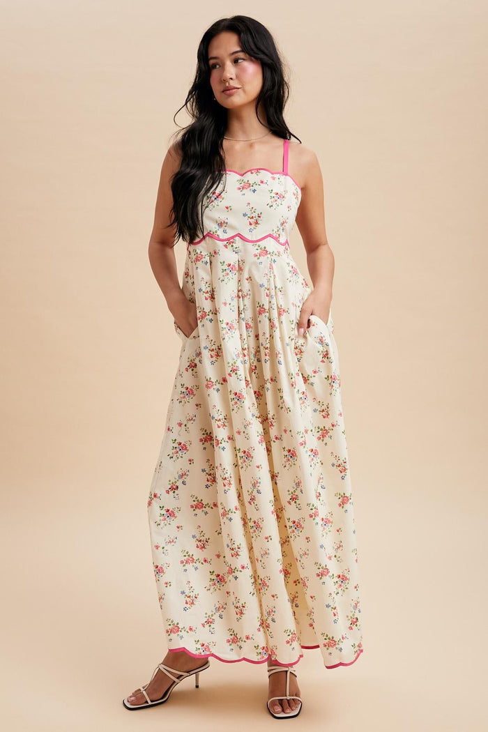 woman wearing a cream floral maxi dress with pink accents and pockets, standing against a neutral background
