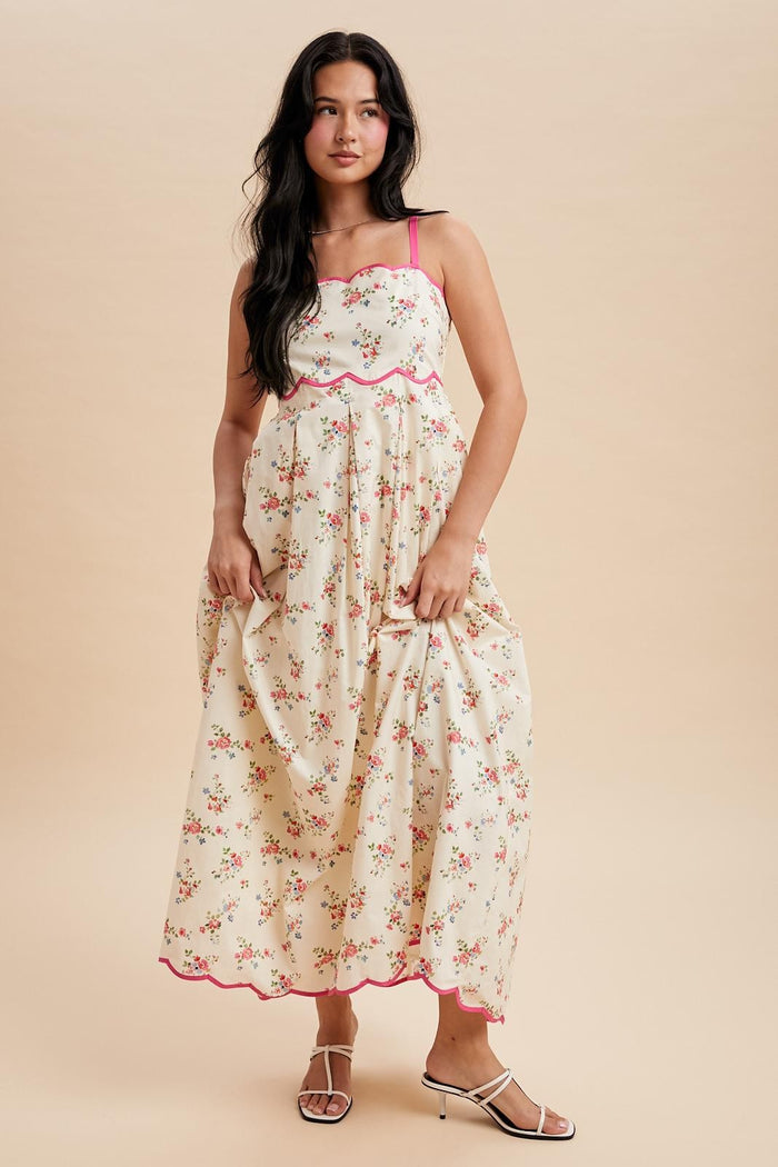 woman wearing a floral maxi dress with pink trim and spaghetti straps, standing against a beige background