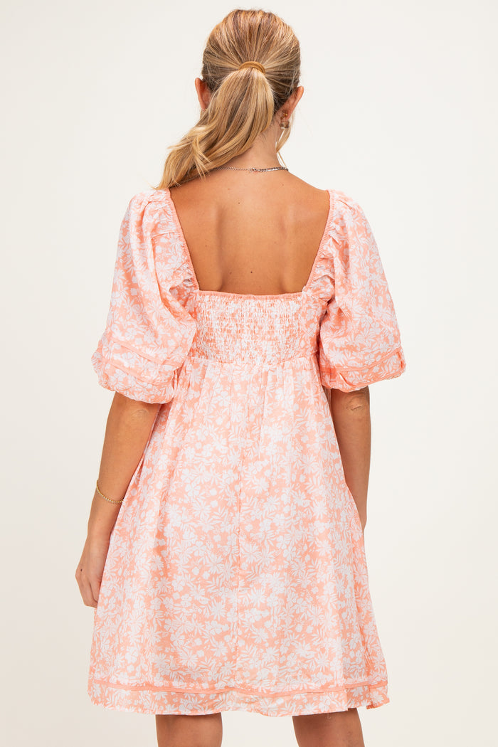 woman wearing a peach floral maternity dress with puff sleeves and a smocked back detail