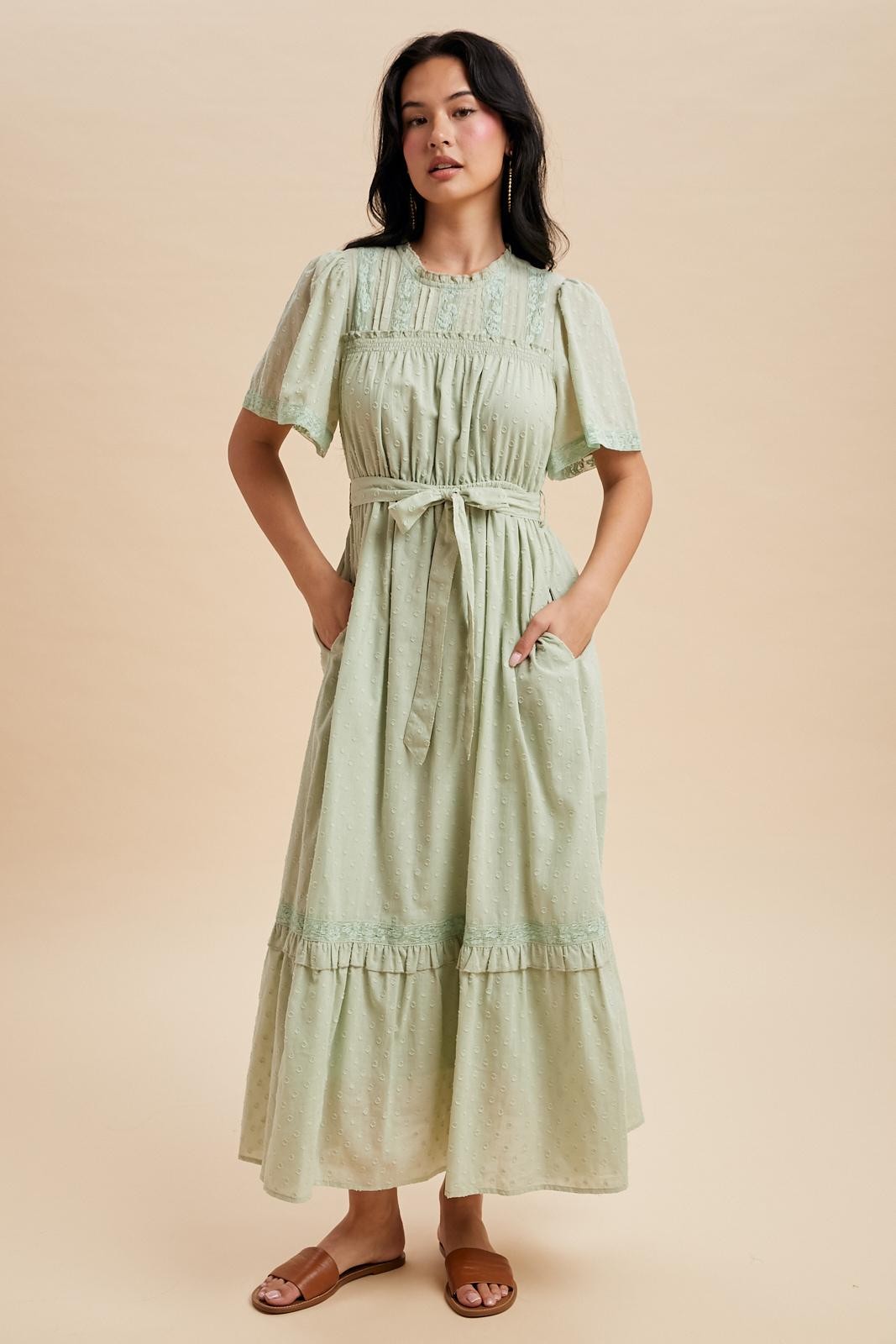 woman wearing a light green maxi dress with short puff sleeves, a cinched waist, and pockets