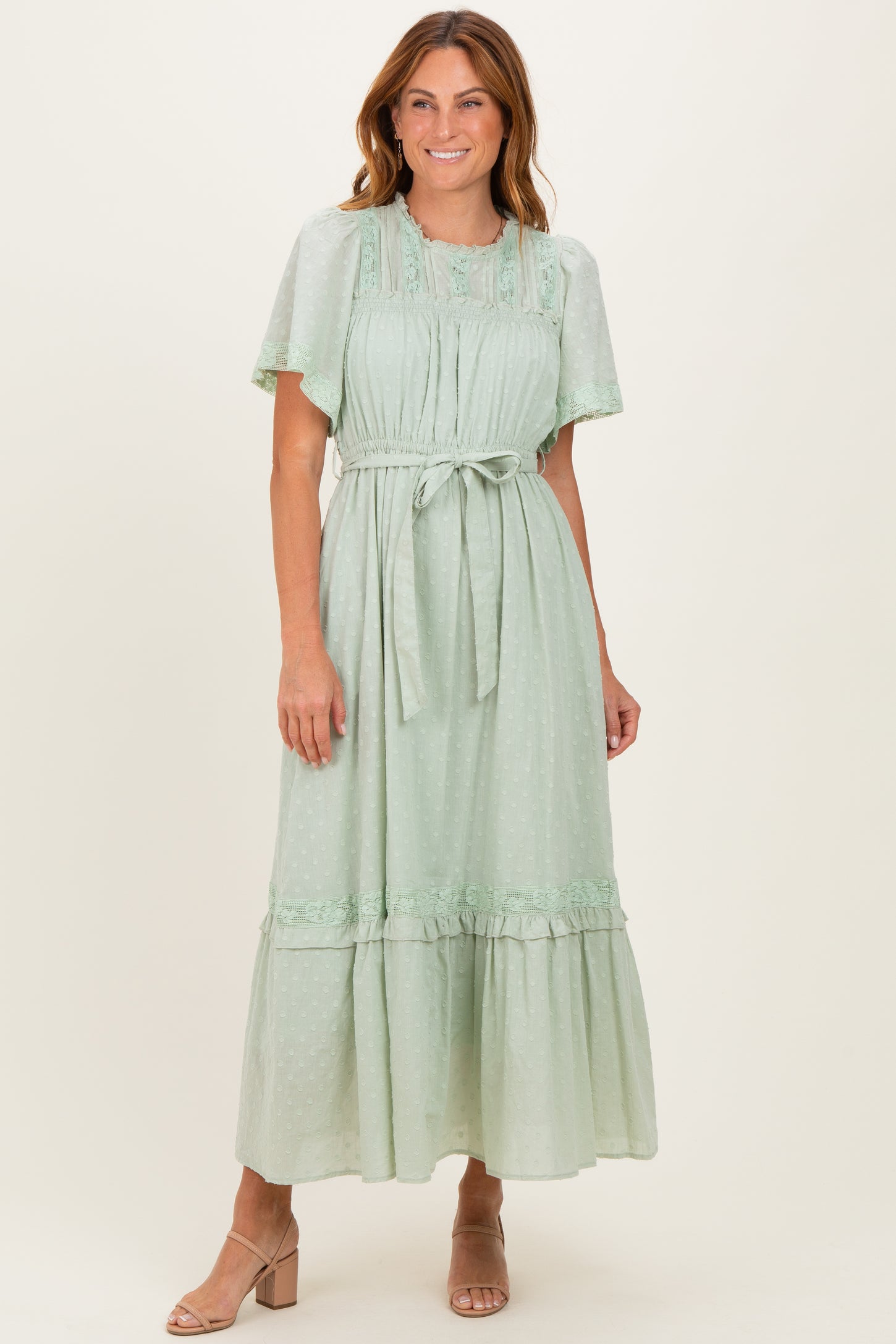 woman wearing a mint green midi dress with flutter sleeves and a tie waist, standing and smiling