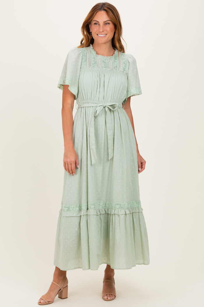 woman wearing a mint green midi dress with flutter sleeves and a tie waist, standing and smiling