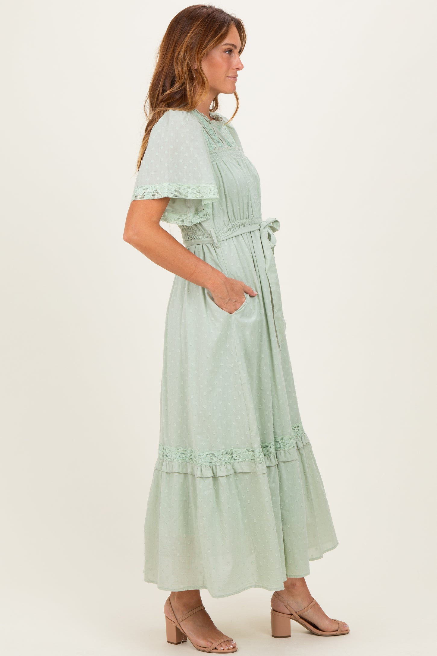 woman wearing a light green maxi dress with ruffle details and pockets, standing sideways with a flowing silhouette