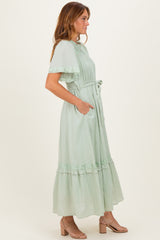 woman wearing a light green maxi dress with ruffle details and pockets, standing sideways with a flowing silhouette
