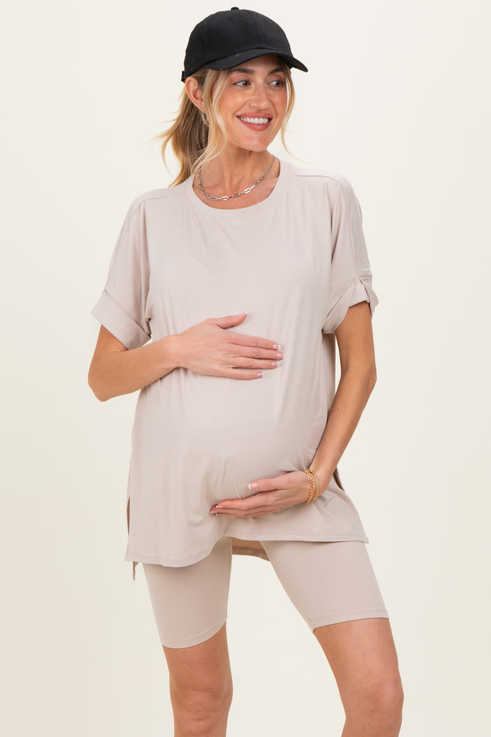 woman wearing a beige maternity top with rolled sleeves and holding her baby bump, paired with matching bike shorts