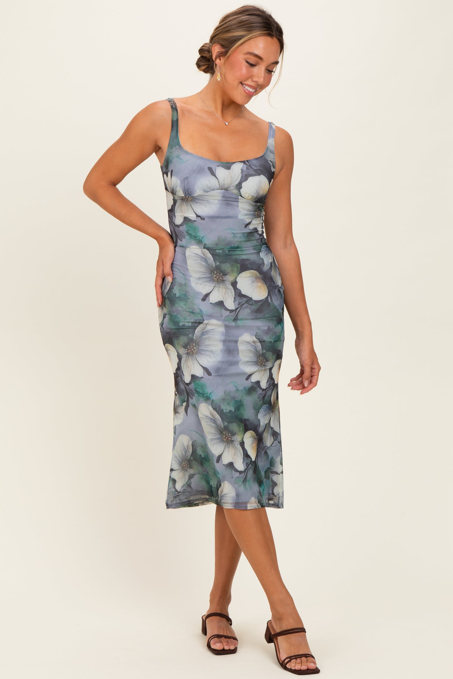 woman wearing a floral midi dress in shades of green and blue with a fitted silhouette and spaghetti straps