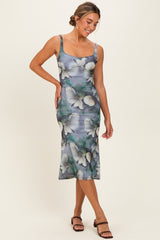 woman wearing a floral midi dress in shades of green and blue with a fitted silhouette and spaghetti straps